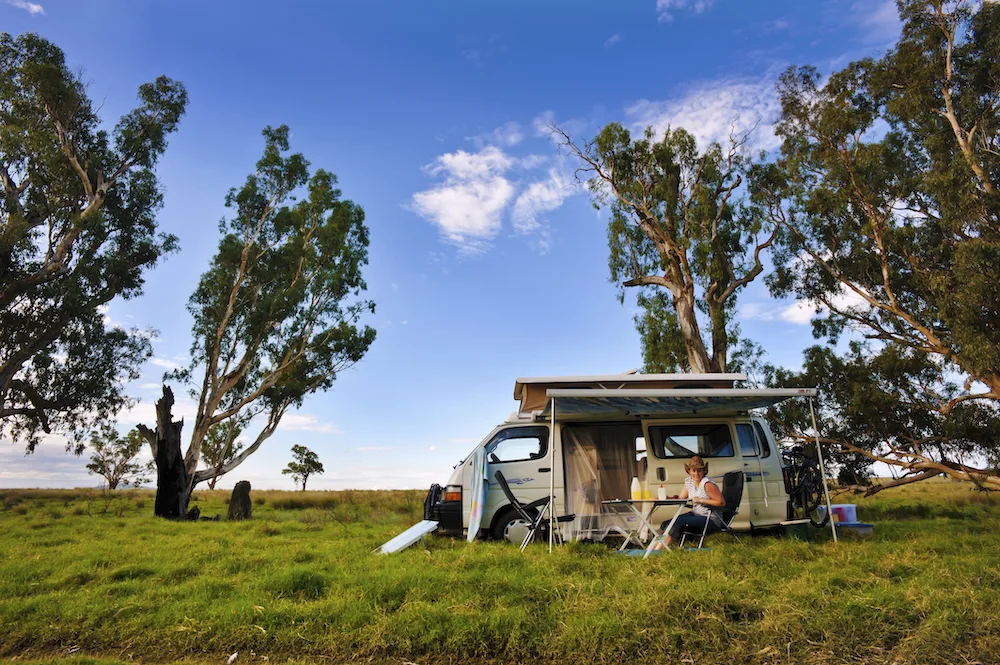 smiling woman next to a campervan in a green field