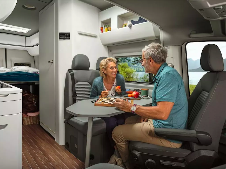 Older couple enjoying a meal at the dinette of a VW Grand California 680 campervan.