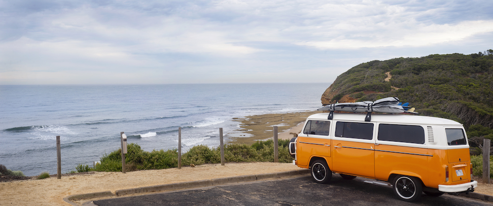 Orange and white VW kombi camper van with surfboards on the roof, parked over looking Bells Beach, Australia.