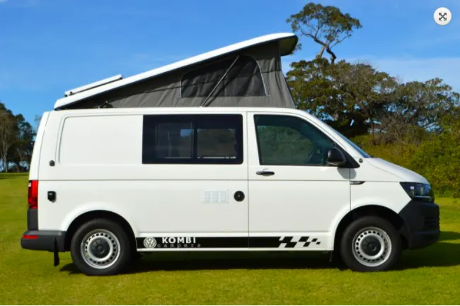 White VW campervan with pop up roof parked outside on grass