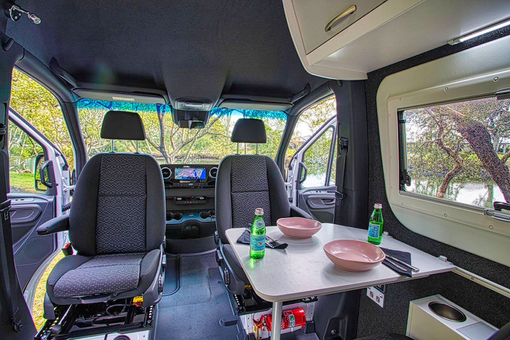 Drivers cab seating area of 4x4 camper van in Australia, showing the captains chairs turned around and dishes on the table.