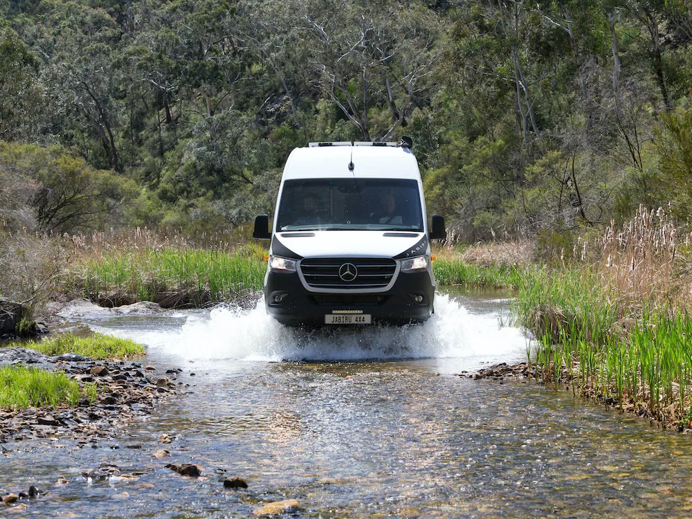 4x4 campervan driving through creek with water splashing up the side of the vehicle.