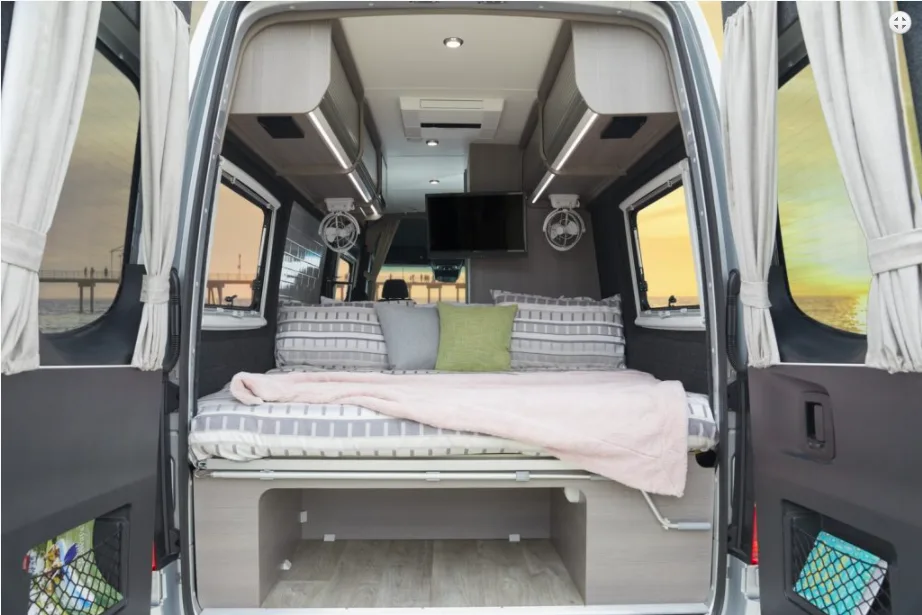 Looking through the rear doors of a Jayco campervan, with the bed made up and storage underneathj.