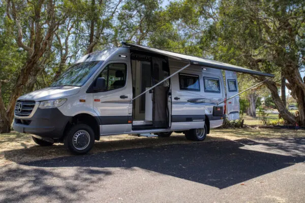 Outside view of a Waratah 4WD campervan parked in the Australian bush, with the awning out and door open.