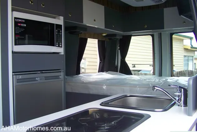 Grey interior of a van showing the kitchen area and the bed.