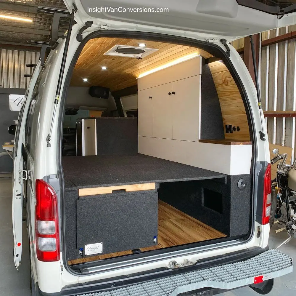 Looking into a converted campervan through the rear door, showing the bed platform and storage on the side wall of the van.