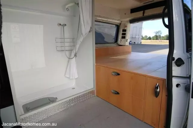 Interior of a campervan conversion showing the bed platform and wet bathroom.