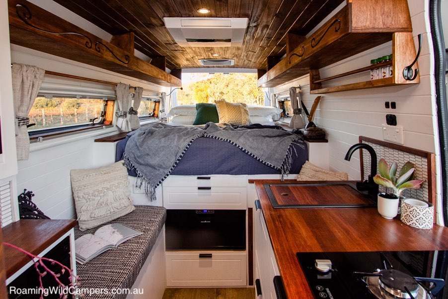 Campervan interior showing a bed, kitchen and sitting area.