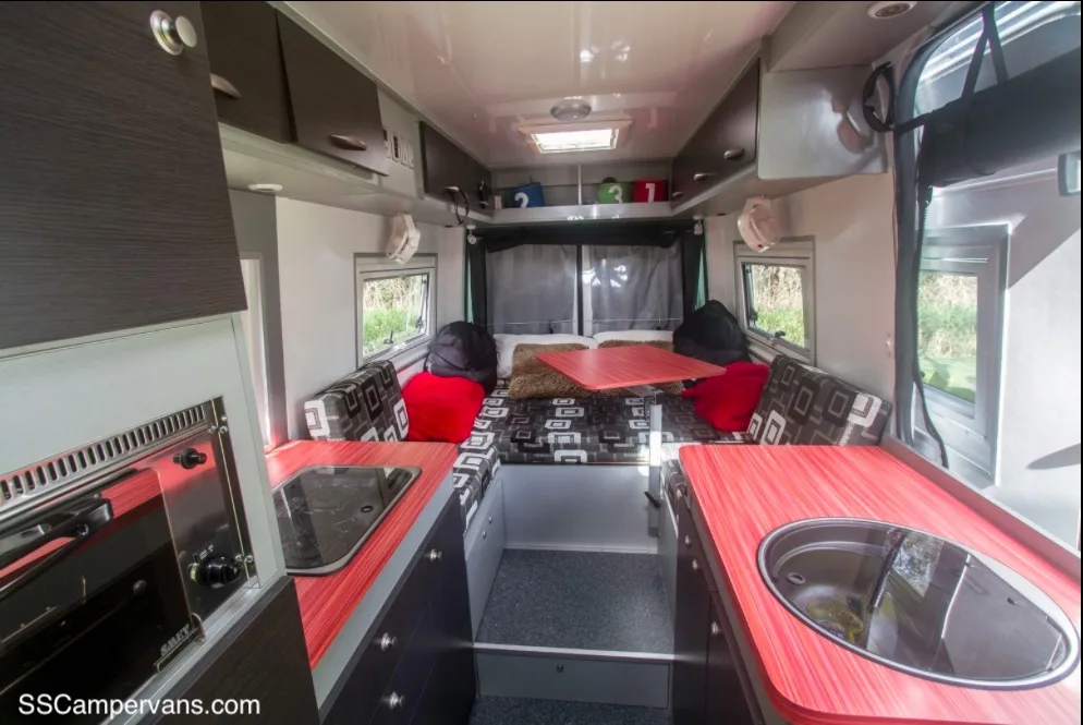 Red and black interior of a campervan showing the kitchen area through to the sleeping area.