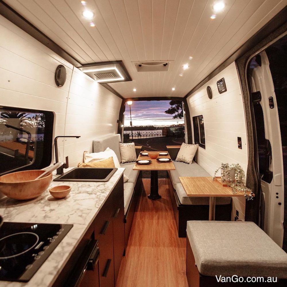 Looking through a campervan dining area to the open back doors showing an rural area at dusk.