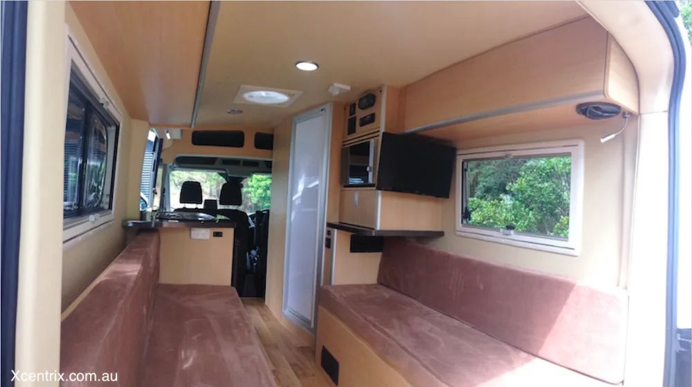 Converted van showing seating area, bathroom and kitchen area.