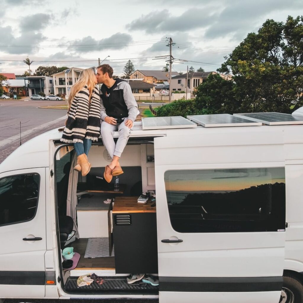 Couple sitting on the roof of a camper van, kissing.