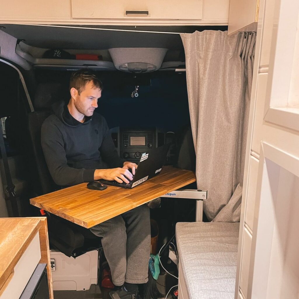 Man working on a laptop in the cab area of a camper van.