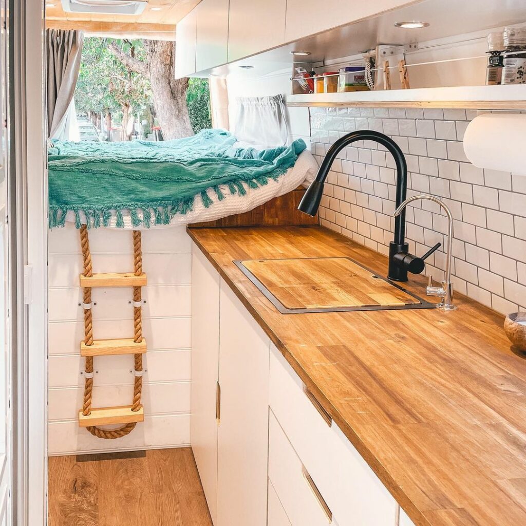 Interior of a converted Sprinter van in Australia, showing the kitchen bench and bed.