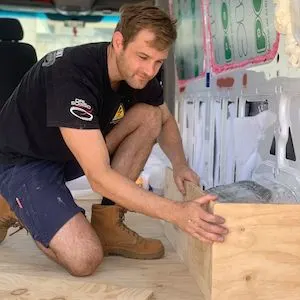 Man kneeling in a van that he is converting to a camper van.