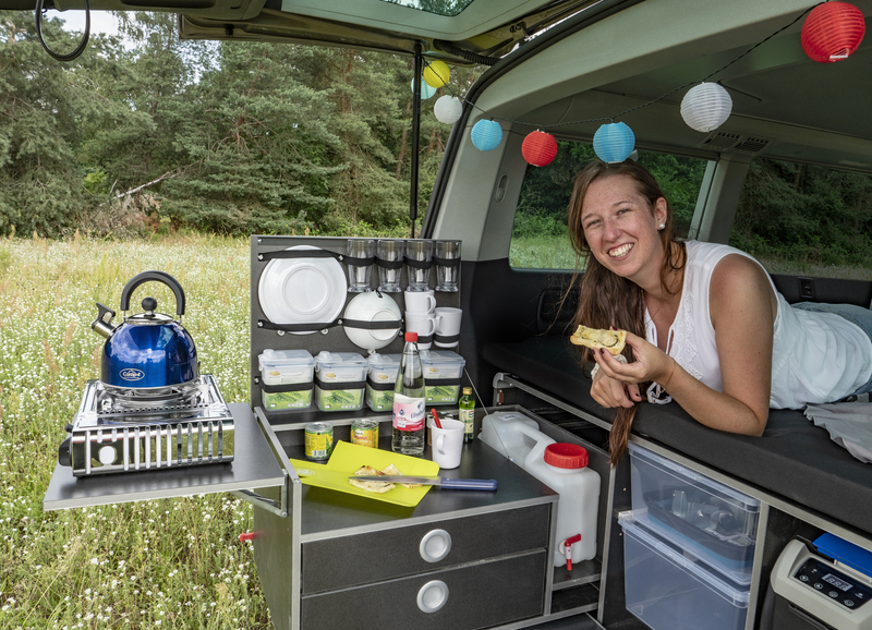 Woman lying in the back of a van on top of a removable camping box.