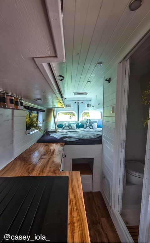 Interior of a converted Mercedes-Benz Sprinter van showing the kitchen and bathroom, and the bed in the back.