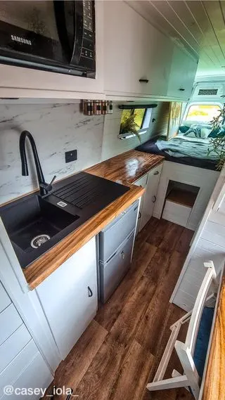 Interior of a converted Mercedes-Benz Sprinter van showing the kitchen area and the bed in the back.