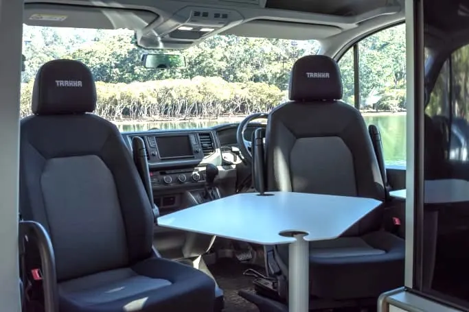 Interior of campervan showing the captains chairs turned around to form a dining area with a removable table between them.