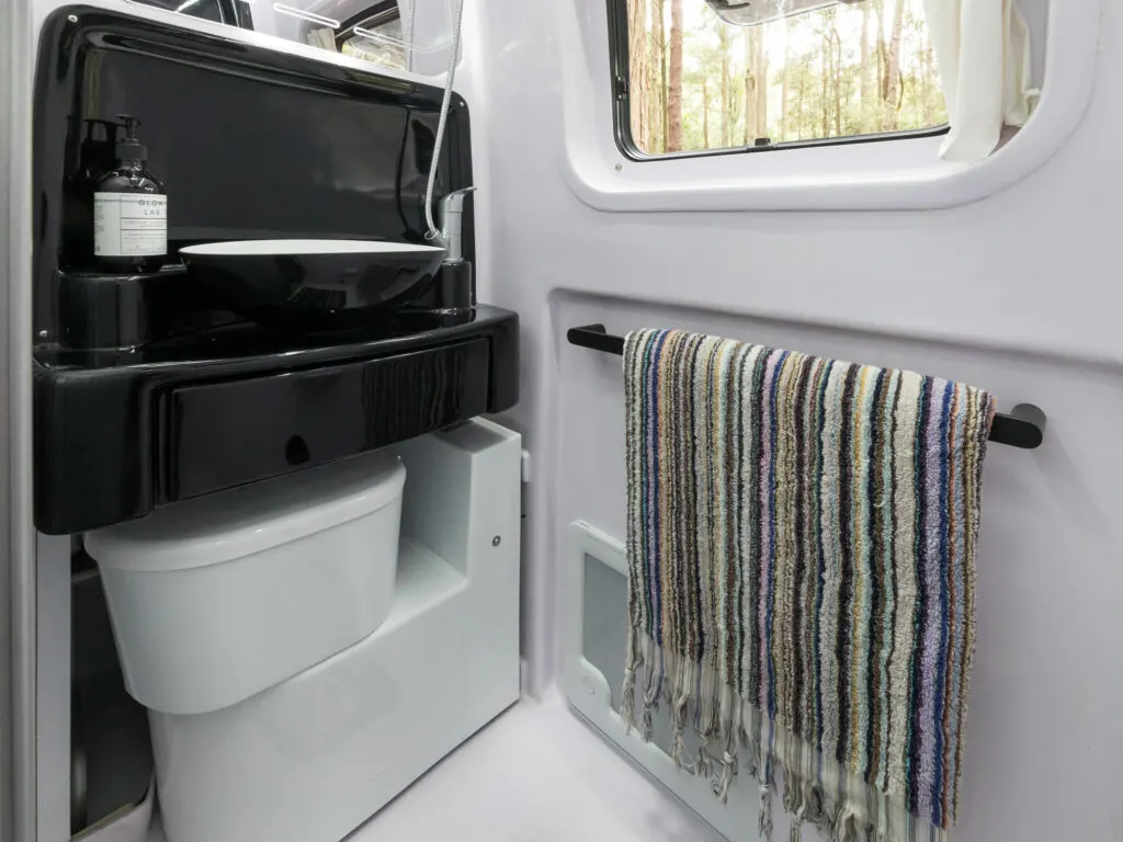 Bathroom of a Trakka campervan that shows the toilet retracted to sit underneath the hand basin.