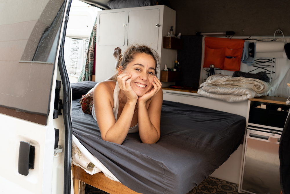 Smiling woman laying on a bed in a camper van.