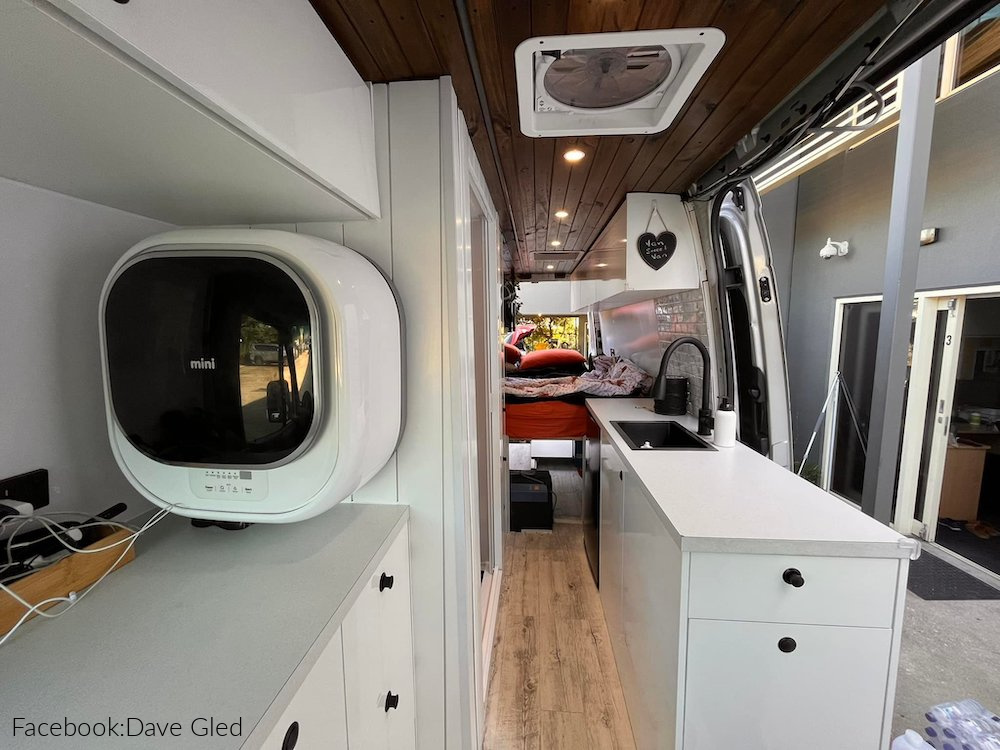 Interior of a campervan showing a mini washing machine mounted to the wall.
