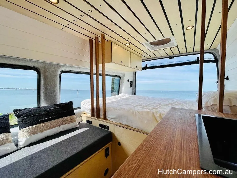 Internal view of a Hutch Campers campervan looking towards the bed in the rear of the van, with a sea view through the windows.