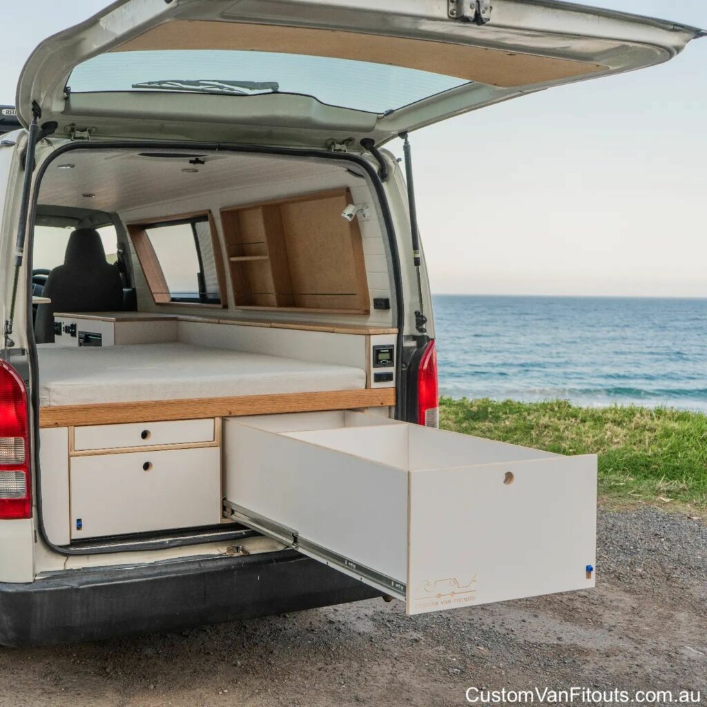 Rear door of a campervan open showing a bed and drawer.
