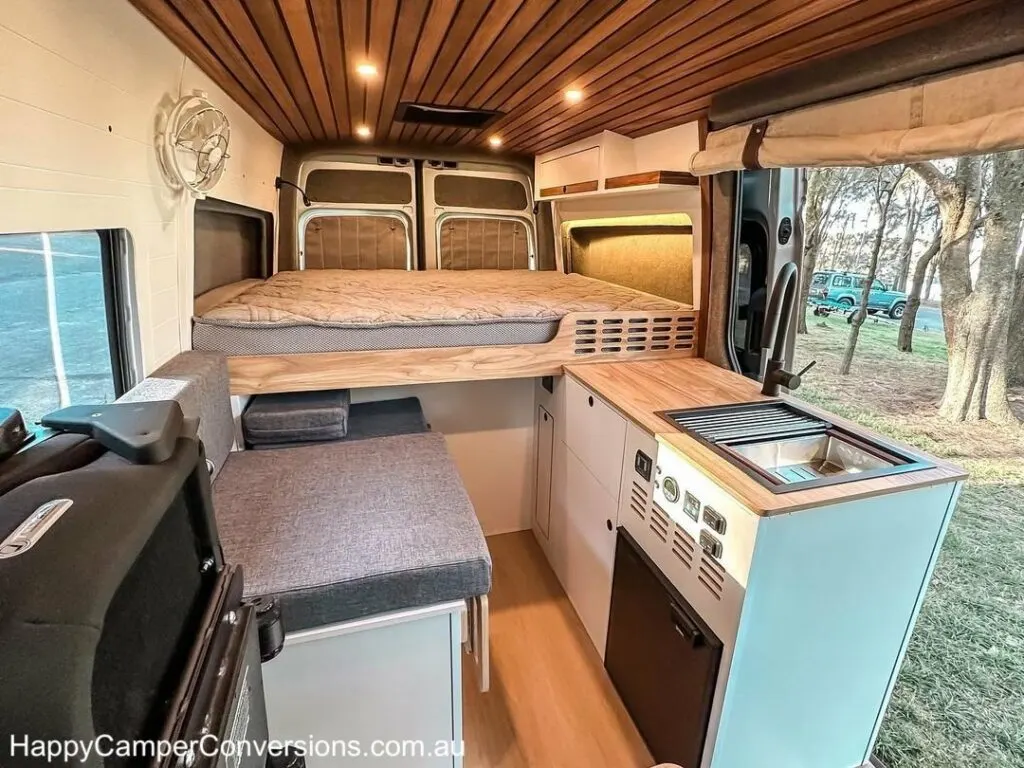 Bed and kitchen area of a campervan by Sydney company Happy Camper Conversions.