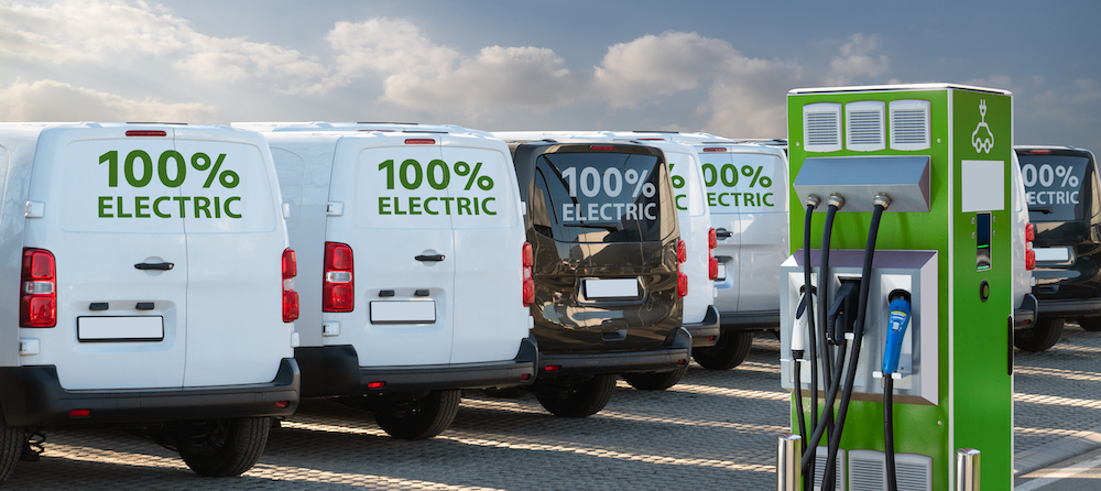 Line of electric vans parked at charging station.