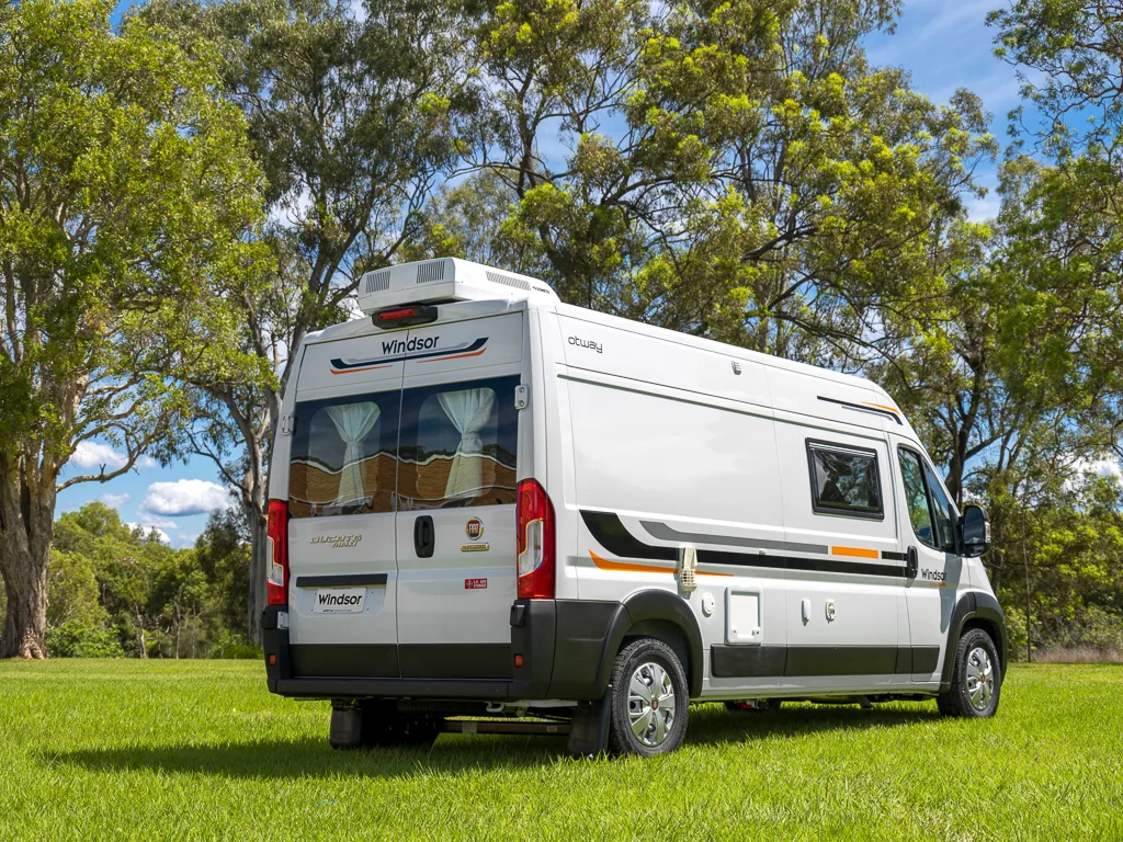 Exterior rear side view of a Windsor Otway campervan parked in a green field.
