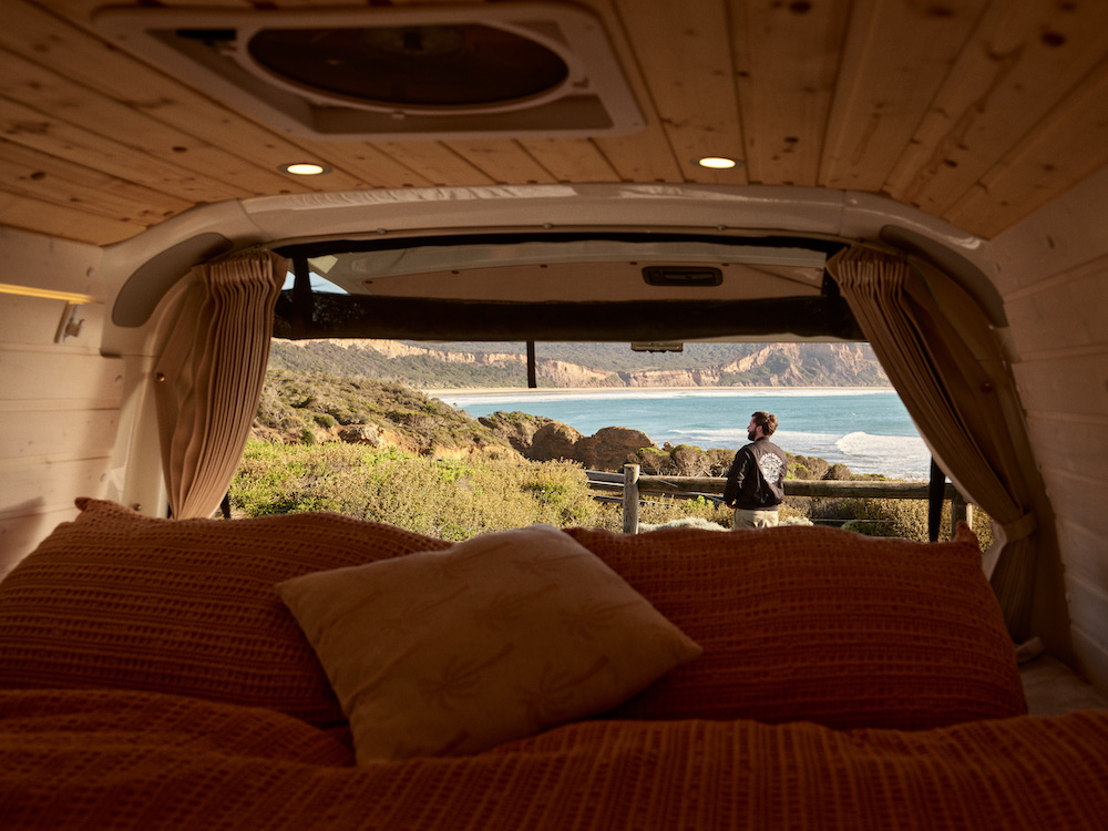 View from the bed inside a camepervan looking through to a beach view.