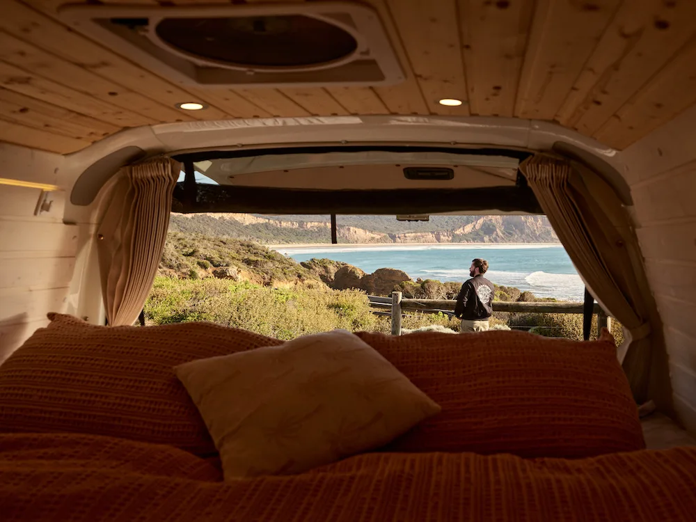 View from the bed inside a camepervan looking through to a beach view.