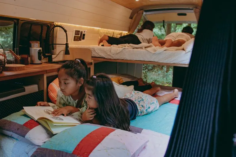 Family of four laying on the beds inside a Toyota Hiace Campervan.
