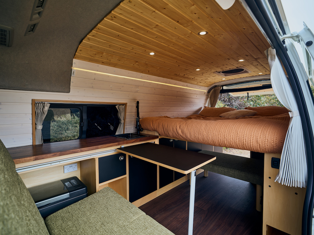 Inside the KumaQ Toyota Hiace campervan showing the seating area and full size bed in the rear.
